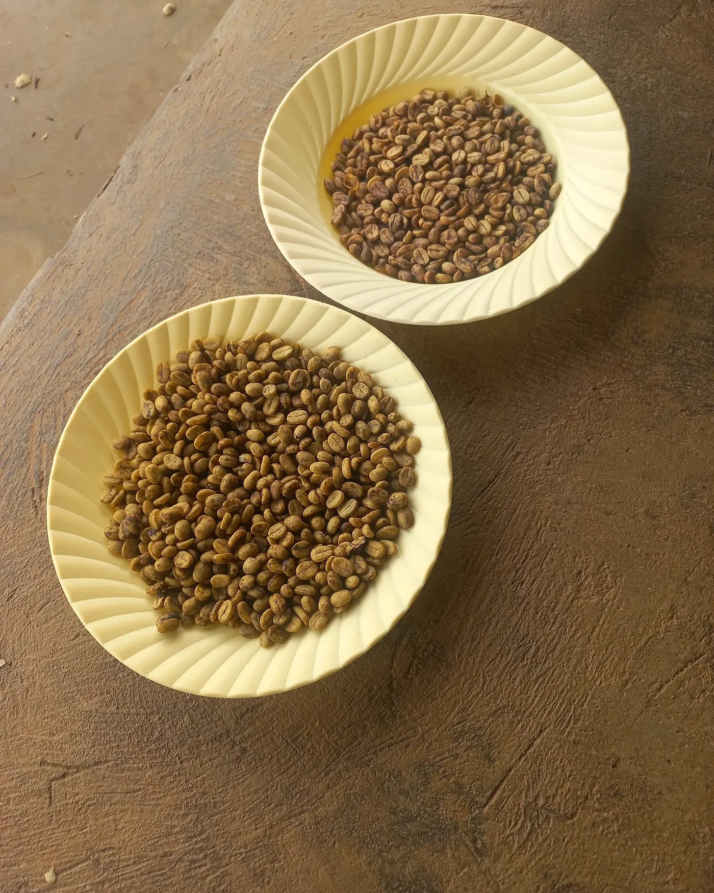 Two bowls of green coffee beans set out on a worn wooden table.